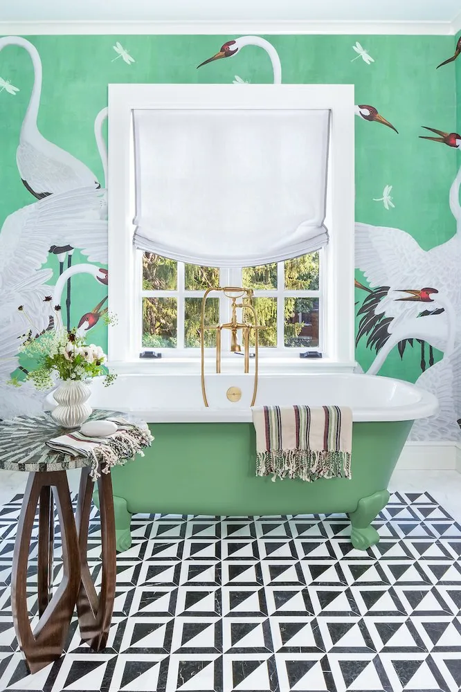 Happy Hollow primary bathroom, emerald clawfoot tub with brass fittings, crane mural wallpaper on green ground, and geometric tile floor. Studio Eckström