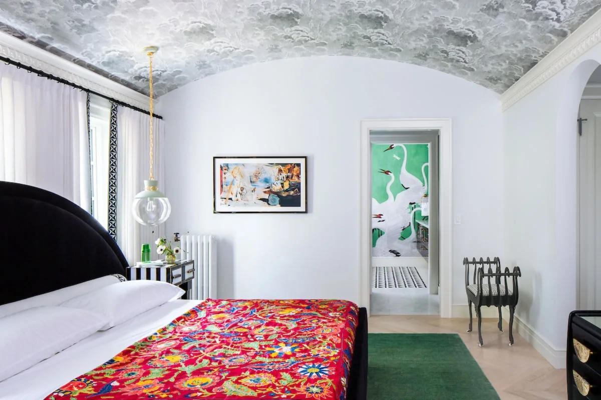 Happy Hollow primary bedroom by Studio Eckström, vaulted ceiling in cloud wallpaper, black arched headboard, vibrant floral coverlet, Omaha Nebraska