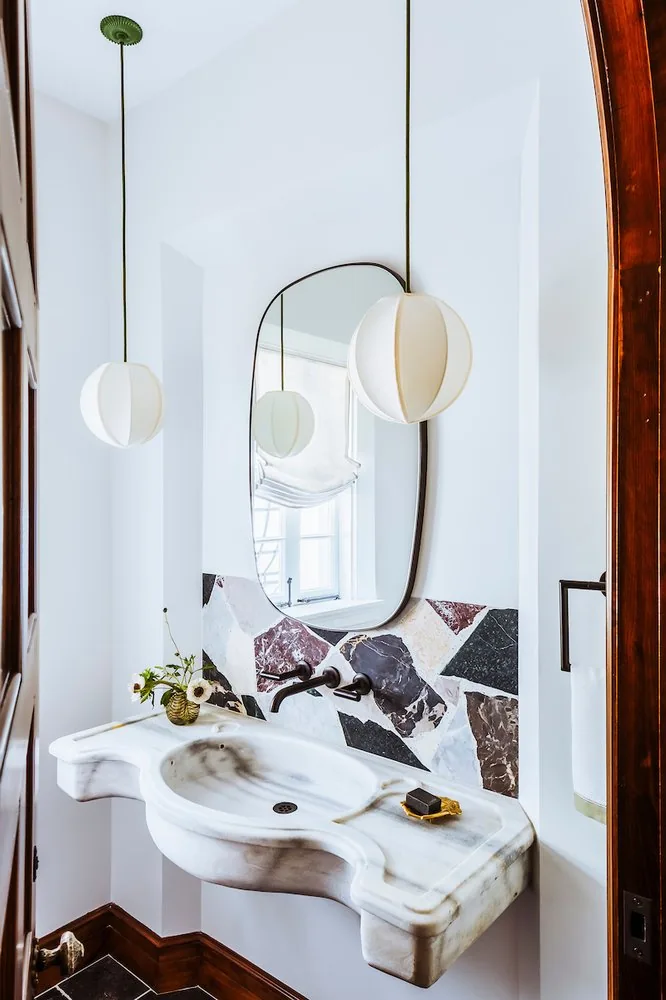 Happy Hollow powder room, antique marble vessel sink, pietra dura backsplash, arched dark-framed mirror, and silk balloon pendants. Studio Eckström