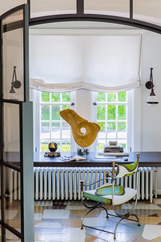 Happy Hollow study framed by a steel and glass arch, black writing desk with organic stone sculpture, and campaign-style chair on a stone floor. Studio Eckström