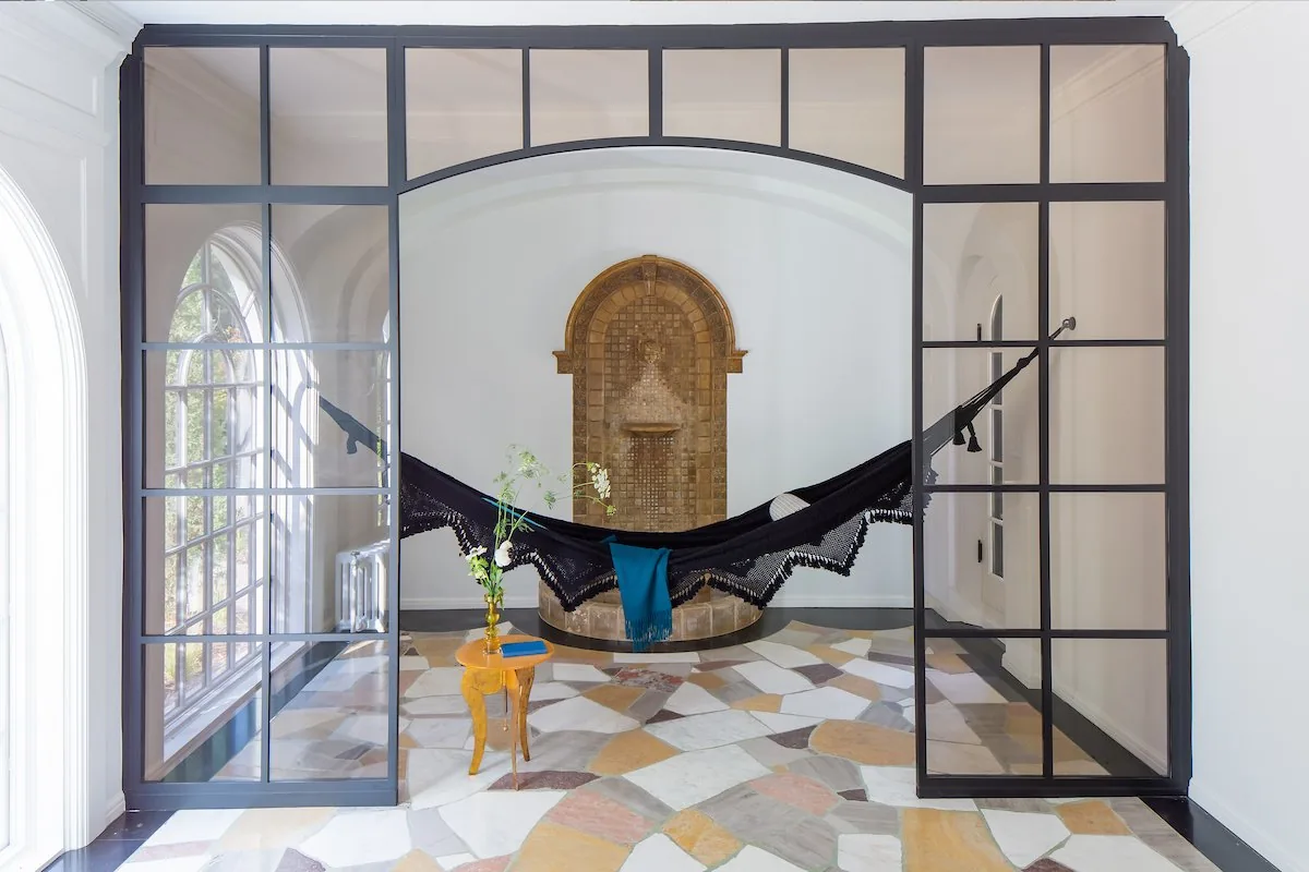 Happy Hollow sunroom, steel and glass arched divider, black hammock with teal throw, mosaic tile fountain alcove, and stone patchwork floor. Studio Eckström