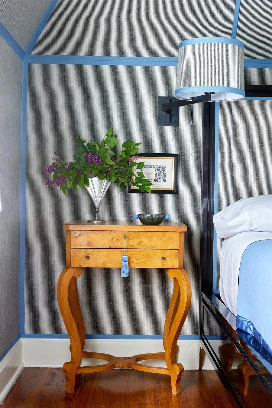 The Ticking Stripe Room, burl Biedermeier nightstand, silver fan vase with lilacs, and ticking stripe walls framed in blue ribbon. The Dundee Remodel, Studio Eckström Omaha