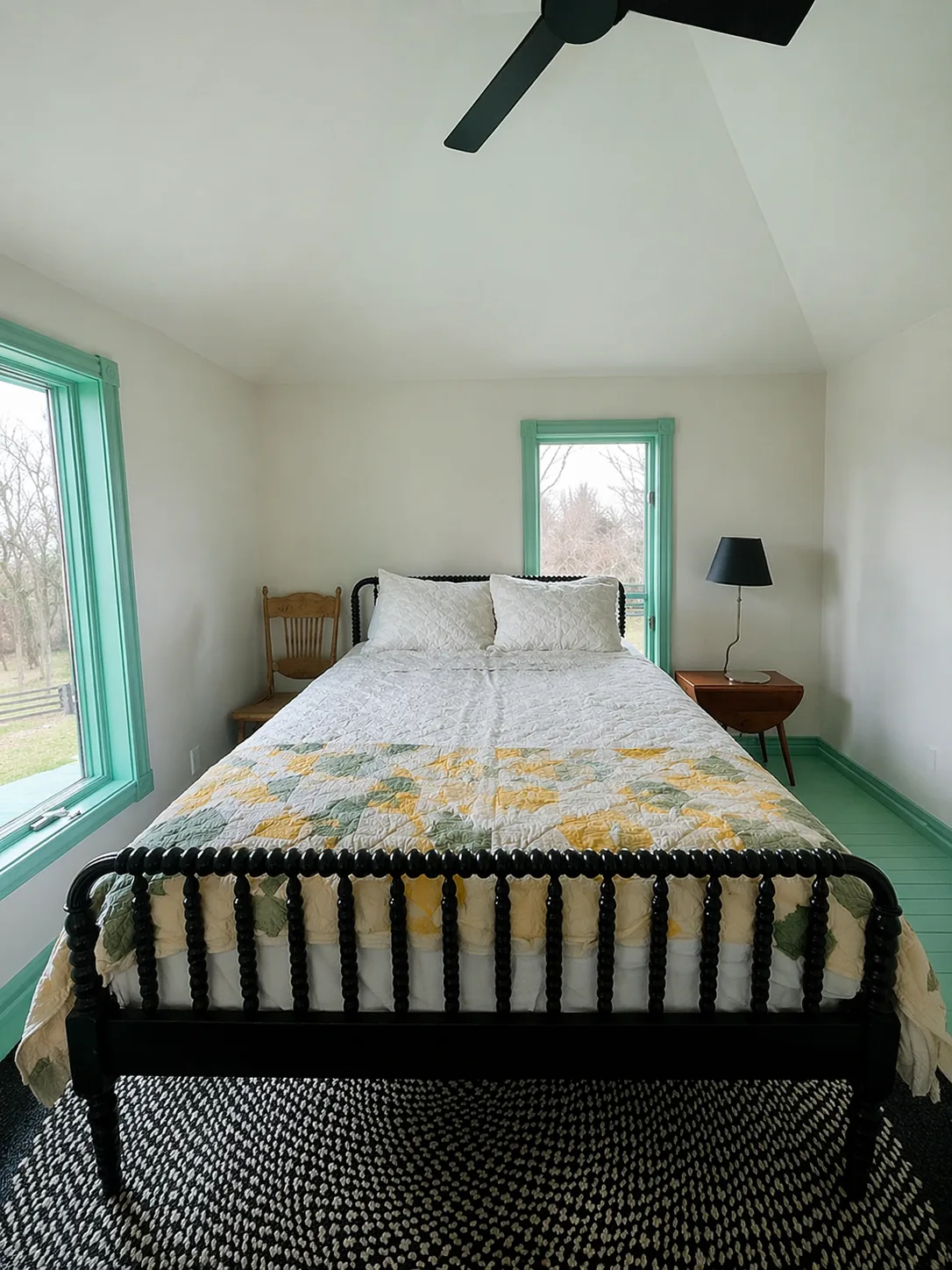 Primary bedroom with black Jenny Lind spool bed, heirloom floral quilt, mint green painted floors, and oversized windows to farm views. Country Equestrian, Studio Eckström