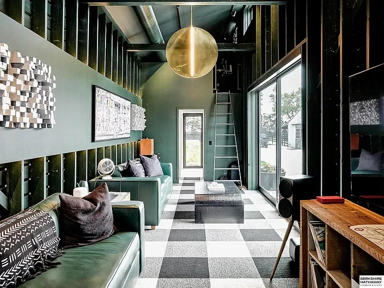 Corn Crib living space, green leather sofa, vinyl record collection, stacked travel books, and bold art on a green corrugated wall. Country Equestrian, Studio Eckström