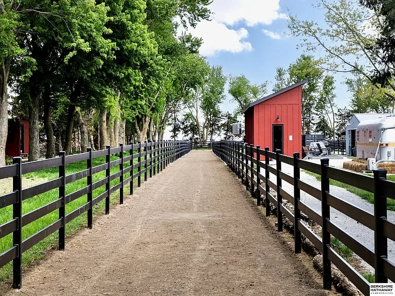 Country Equestrian property drive, black rail fencing along a gravel lane to a red outbuilding, open Nebraska farmland. Studio Eckström, Kenard Nebraska 2023