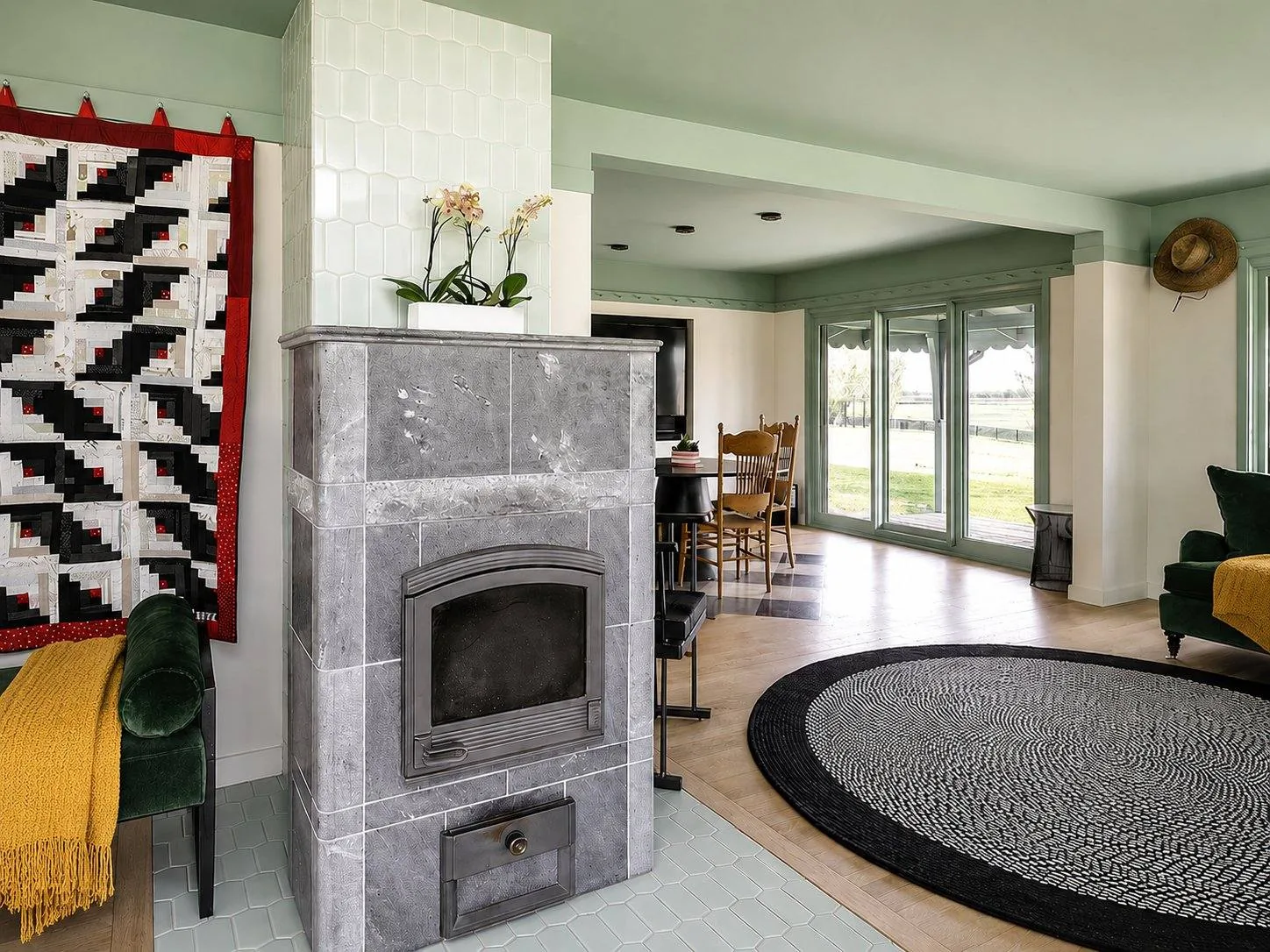Living room with marble tile fireplace surround, mint green walls, folk art quilt above the mantle, and herringbone wood floor. Country Equestrian, Studio Eckström