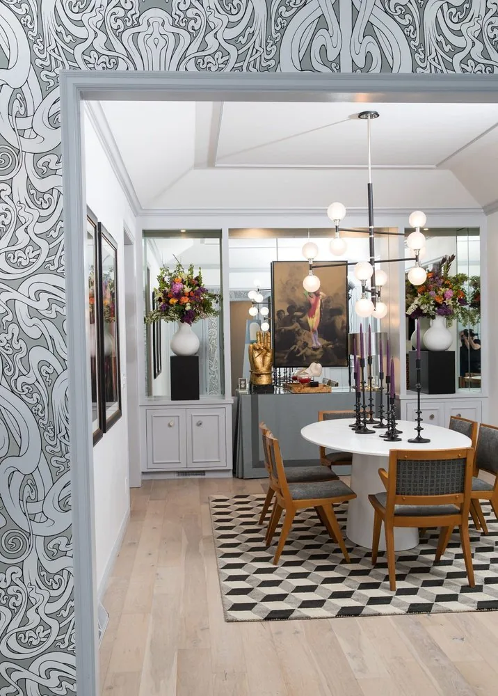 The Regency Refresh dining room from the foyer, bold black and white swirl wallpaper, white tulip table, iron candlesticks, and multi-globe pendant. Studio Eckström Omaha