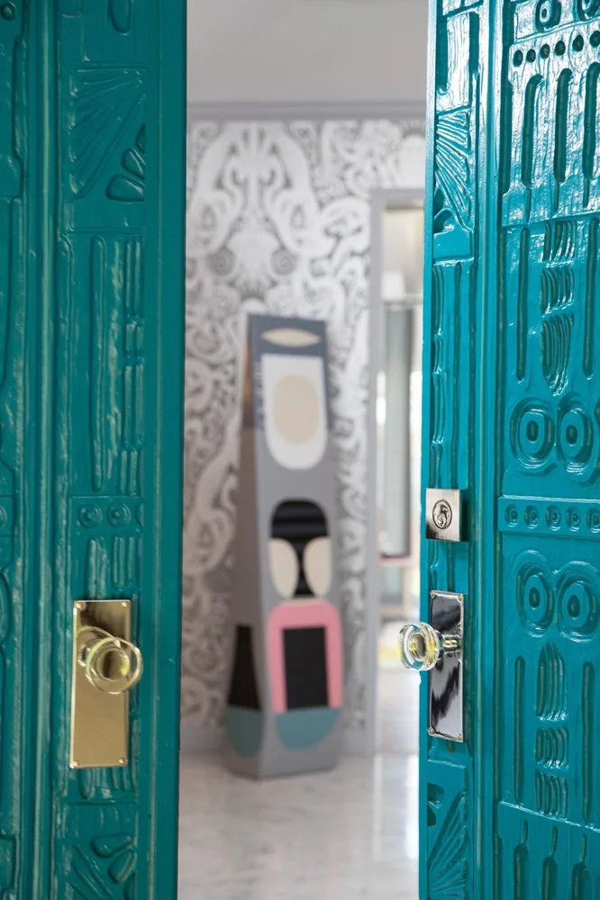The Regency Refresh entry, teal lacquered ornate carved double doors, bold graphic black and white wallpaper beyond, and sculptural artwork on a pedestal. Studio Eckström Omaha