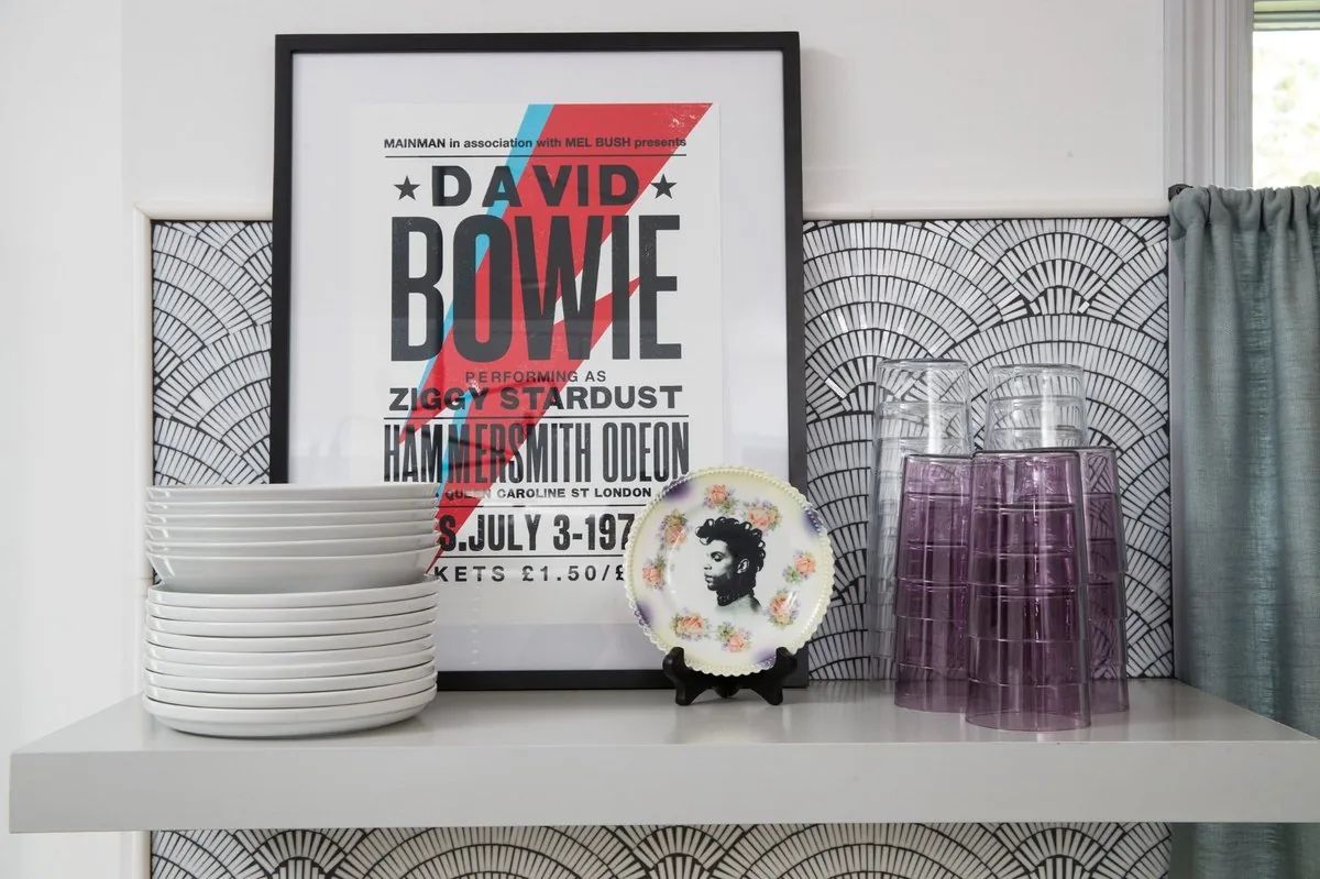 The Regency Refresh kitchen shelving, David Bowie concert poster, Prince portrait plate, white ceramics, and black and white scallop tile. Studio Eckström Omaha