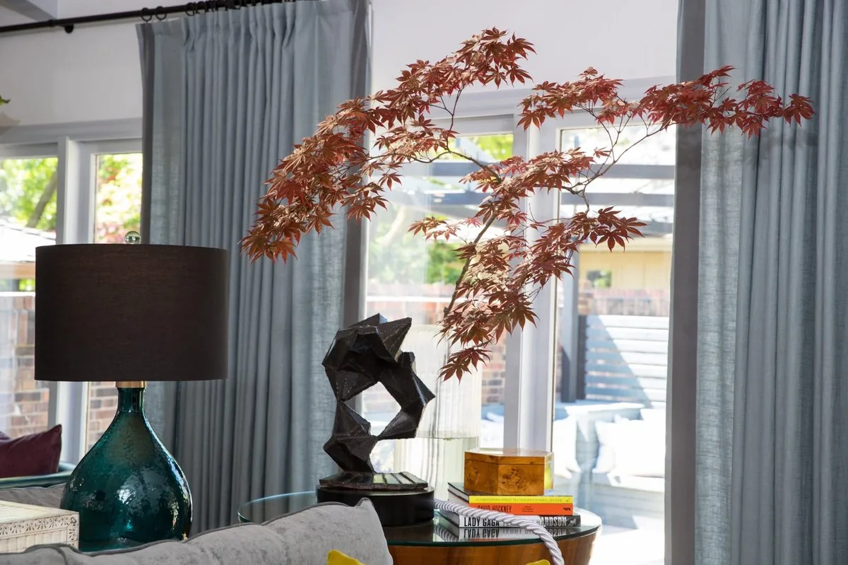 The Regency Refresh living room console, Japanese maple branch in glass vase, teal ceramic lamp, bronze sculpture, and art books. Studio Eckström Omaha