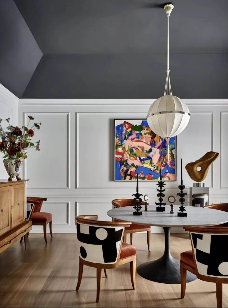 The Architectural Digest Townhome dining room, dark coffered ceiling, white wainscot, Saarinen tulip marble table, patterned chairs, and abstract painting. Studio Eckström 2023