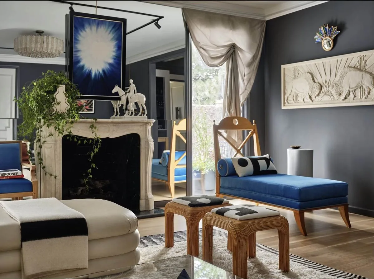 The Architectural Digest Townhome drawing room fireplace wall, deep blue-grey walls, white marble mantel, blue velvet daybed, and draped silk curtains. Studio Eckström 2023