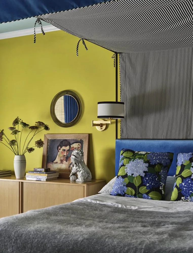 The Architectural Digest Townhome guest bedroom, acid yellow walls, cobalt upholstered headboard, and black and white striped four-poster canopy. Studio Eckström 2023
