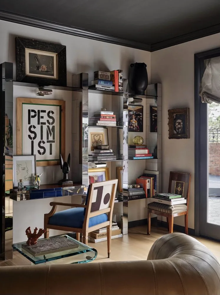 The Architectural Digest Townhome library shelving, smoked mirrored shelves of art books, blue velvet Louis XVI chair, and glass sculptural coffee table. Studio Eckström 2023