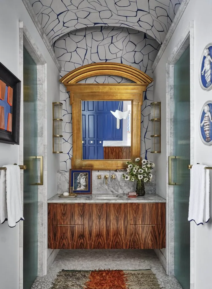The Architectural Digest Townhome primary bathroom, vaulted arch in pebble-pattern wallpaper, gilded mirror, macassar floating vanity, and pebble mosaic floor. Studio Eckström 2023