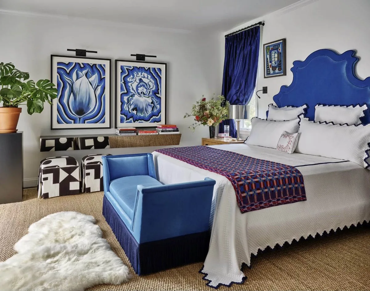 The Architectural Digest Townhome primary bedroom, cobalt blue baroque upholstered headboard, deep blue silk curtains, and paired botanical prints. Studio Eckström 2023