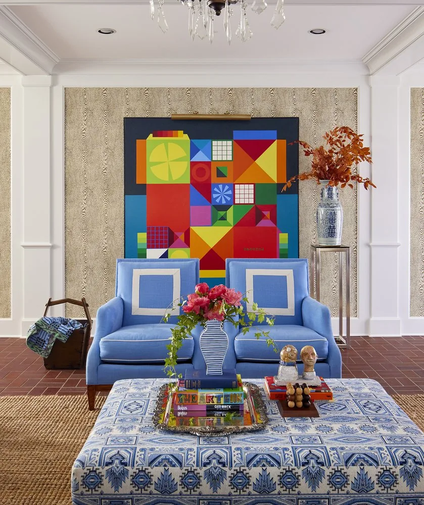 The Westchester family room seating, two periwinkle armchairs facing a bold primary-color geometric painting, with printed ottoman and crystal chandelier. Studio Eckström Omaha