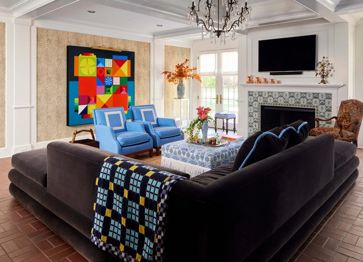 The Westchester family room, charcoal velvet sectional, paired blue armchairs, bold geometric painting, Delft tile fireplace, and terra cotta herringbone floor. Studio Eckström Omaha