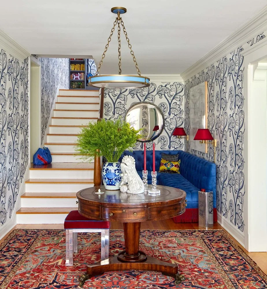 The Westchester foyer, deep navy botanical wallpaper, blue drum pendant, cobalt tufted sofa, antique mahogany center table, and Persian rug. Studio Eckström Omaha
