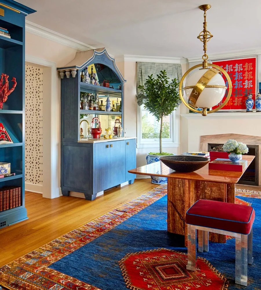 The Westchester library bar corner, custom blue painted bar hutch with arched hood, marble top table, red velvet Lucite stools, and armillary sphere pendant. Studio Eckström Omaha